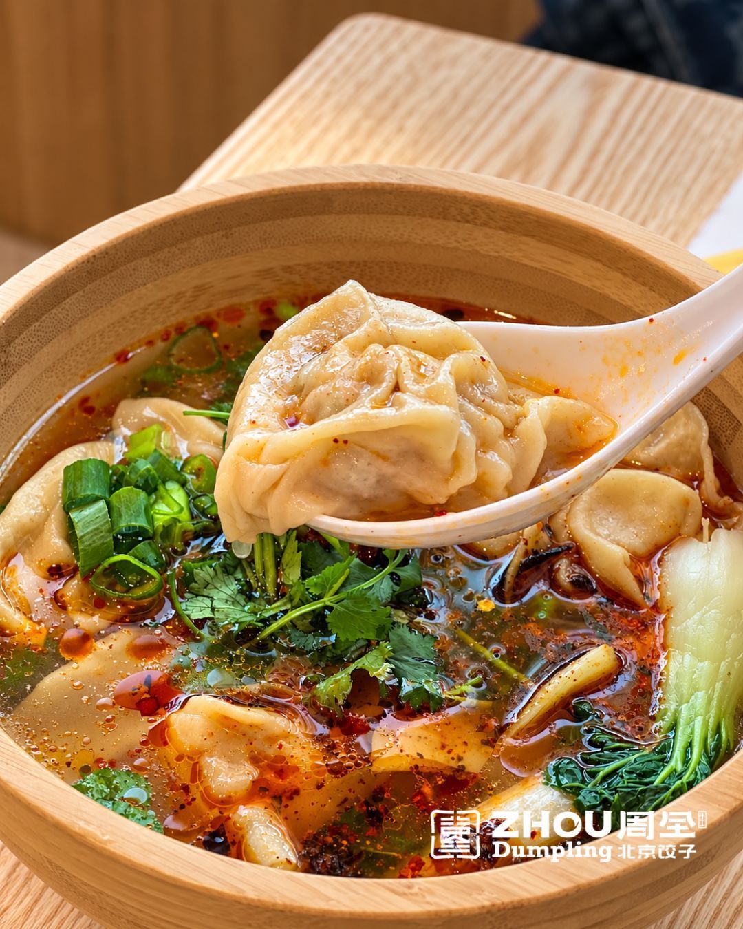 Raviolis chinois dans un bol en bois avec bouillon épicé, coriandre, oignons verts et légumes verts frais.